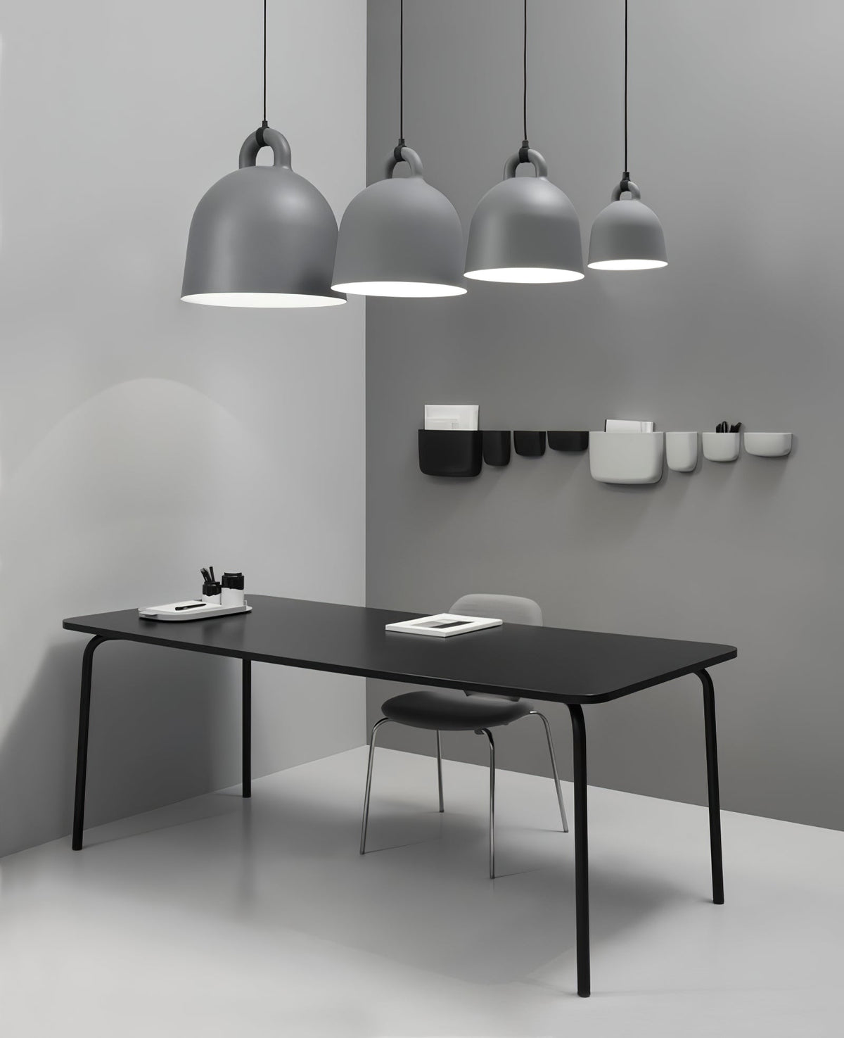 Four grey Clérachic bell pendants, graduated in size, hang over a black table, with wall pockets on the grey corner wall.