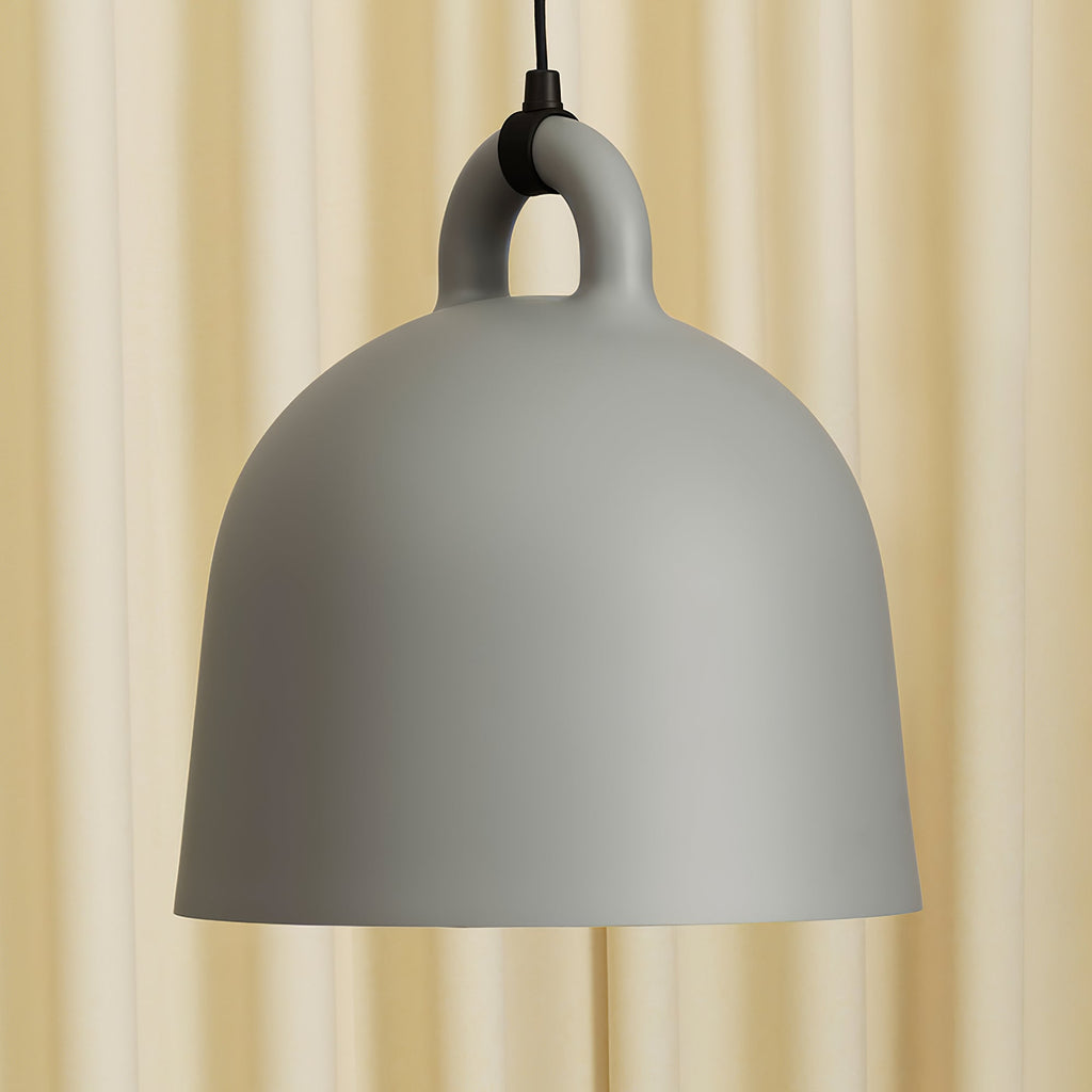 Close view of a grey Clérachic bell pendant and its loop handle, set against a soft cream curtain.
