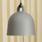 Close view of a grey Clérachic bell pendant and its loop handle, set against a soft cream curtain.