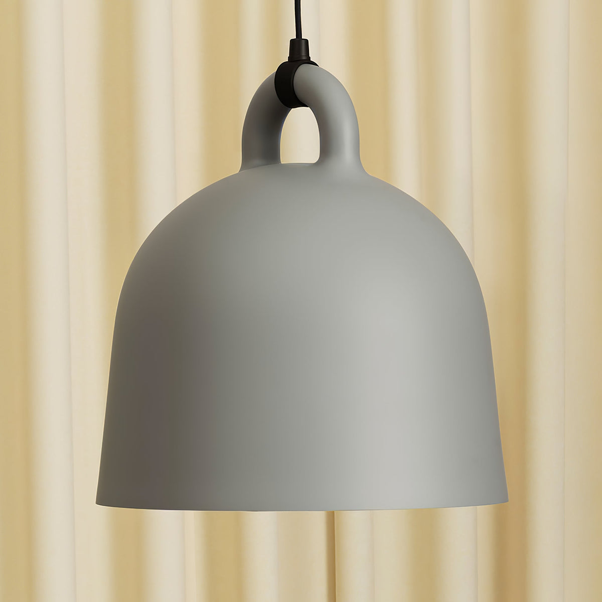 Close view of a grey Clérachic bell pendant and its loop handle, set against a soft cream curtain.