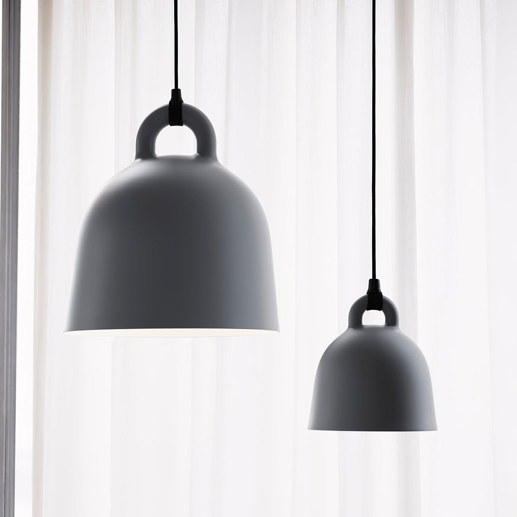 Two grey Clérachic bell pendants of different sizes hang by a sheer white curtain, lit from behind with a soft glow.