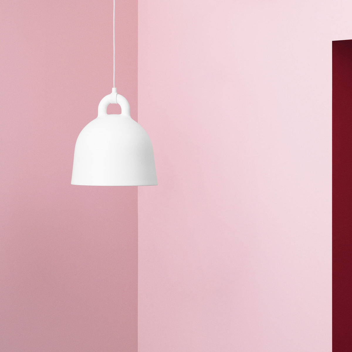 A white Clérachic bell pendant on a white cord hangs in a pink corner beside a deep red door.