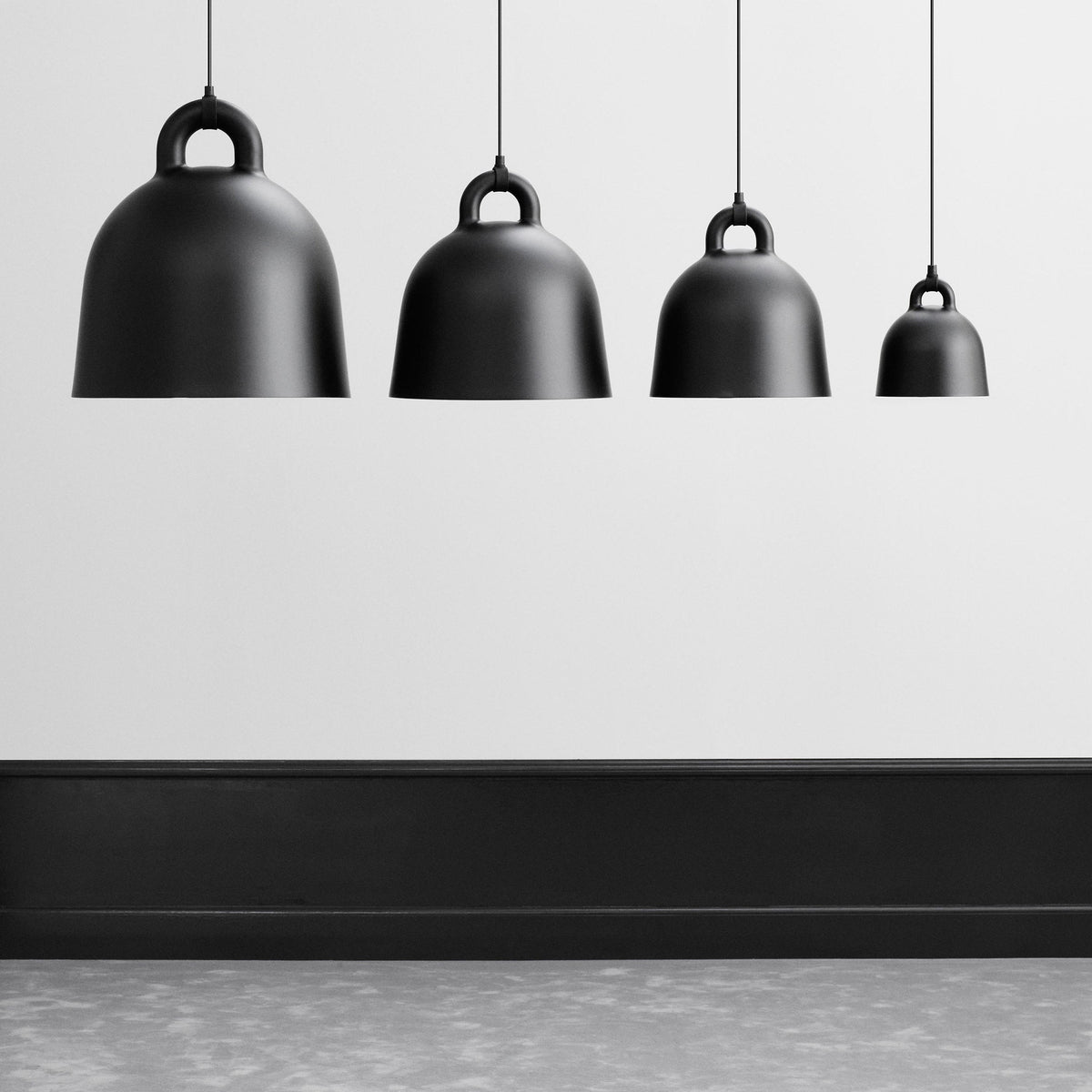 Four black Clérachic bell pendants of graduated size hang above a black skirting board on a pale grey wall.