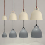 Eight Clérachic bell pendants in four sizes, in sand and grey, hang in two rows on a soft grey backdrop.