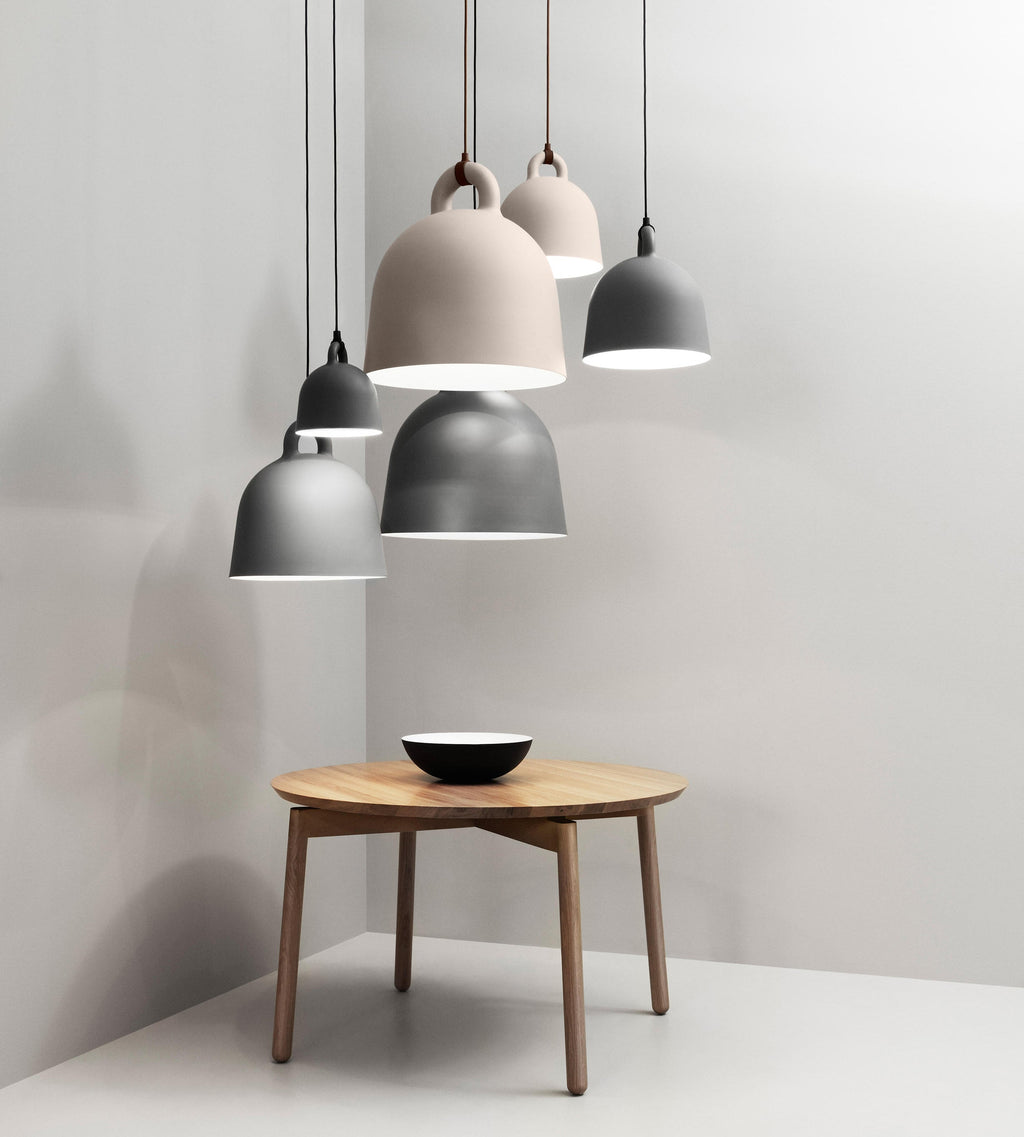 Grey and sand-coloured Clérachic bell pendants cluster in a pale corner above a round wooden table with a black-and-white bowl.