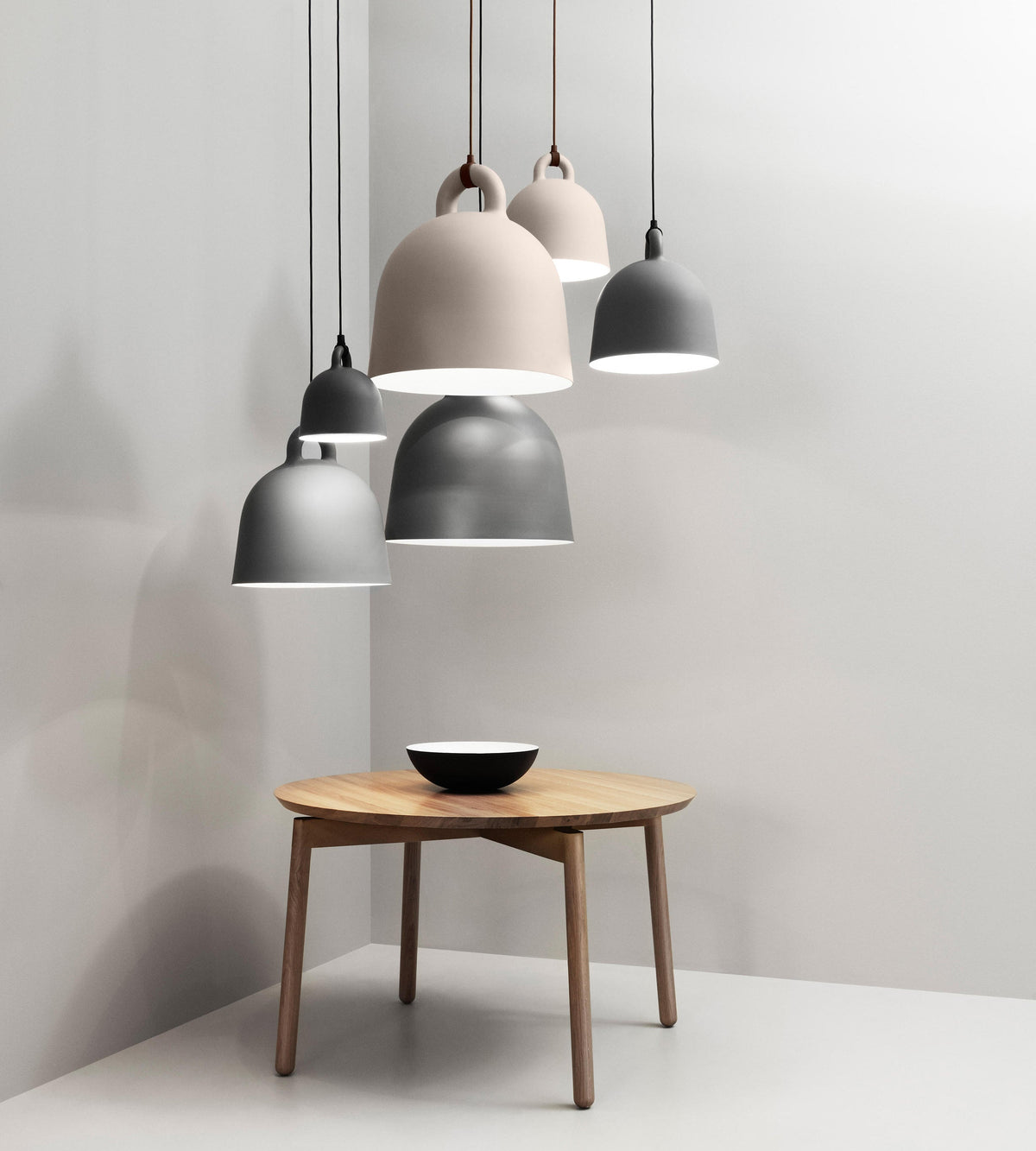 Grey and sand-coloured Clérachic bell pendants cluster in a pale corner above a round wooden table with a black-and-white bowl.