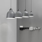 Four grey Clérachic bell pendants in graduated sizes hang on a grey wall, above a row of black and white wall pockets.