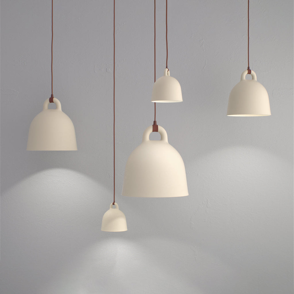 Four cream Clérachic bell pendants at different heights glow against a grey wall, casting soft pools of light.