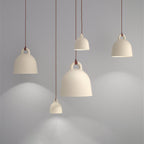 Four cream Clérachic bell pendants at different heights glow against a grey wall, casting soft pools of light.