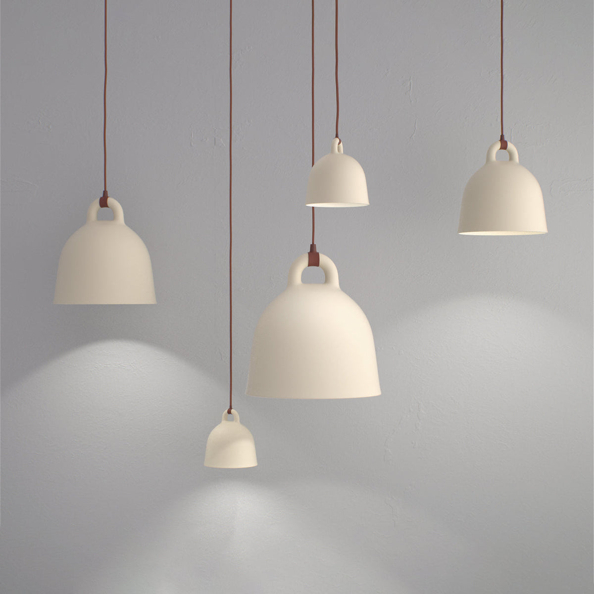 Four cream Clérachic bell pendants at different heights glow against a grey wall, casting soft pools of light.
