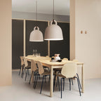 Two sand-coloured Clérachic bell pendants hang over a pale wood dining table, set against a dark mesh wall and peach panels.