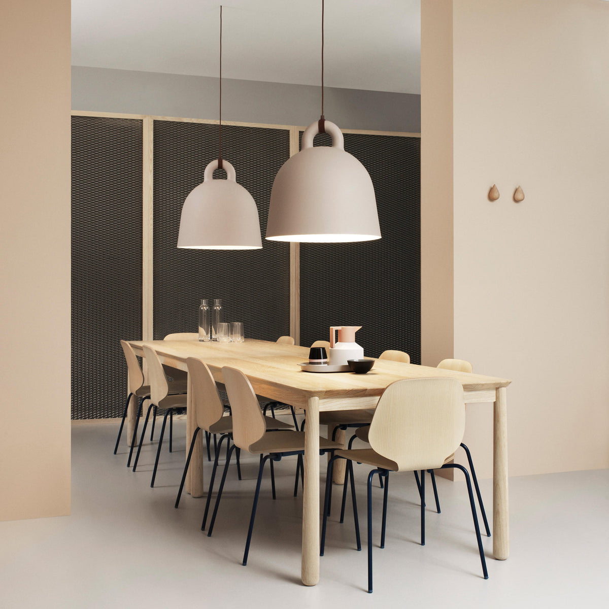 Two sand-coloured Clérachic bell pendants hang over a pale wood dining table, set against a dark mesh wall and peach panels.