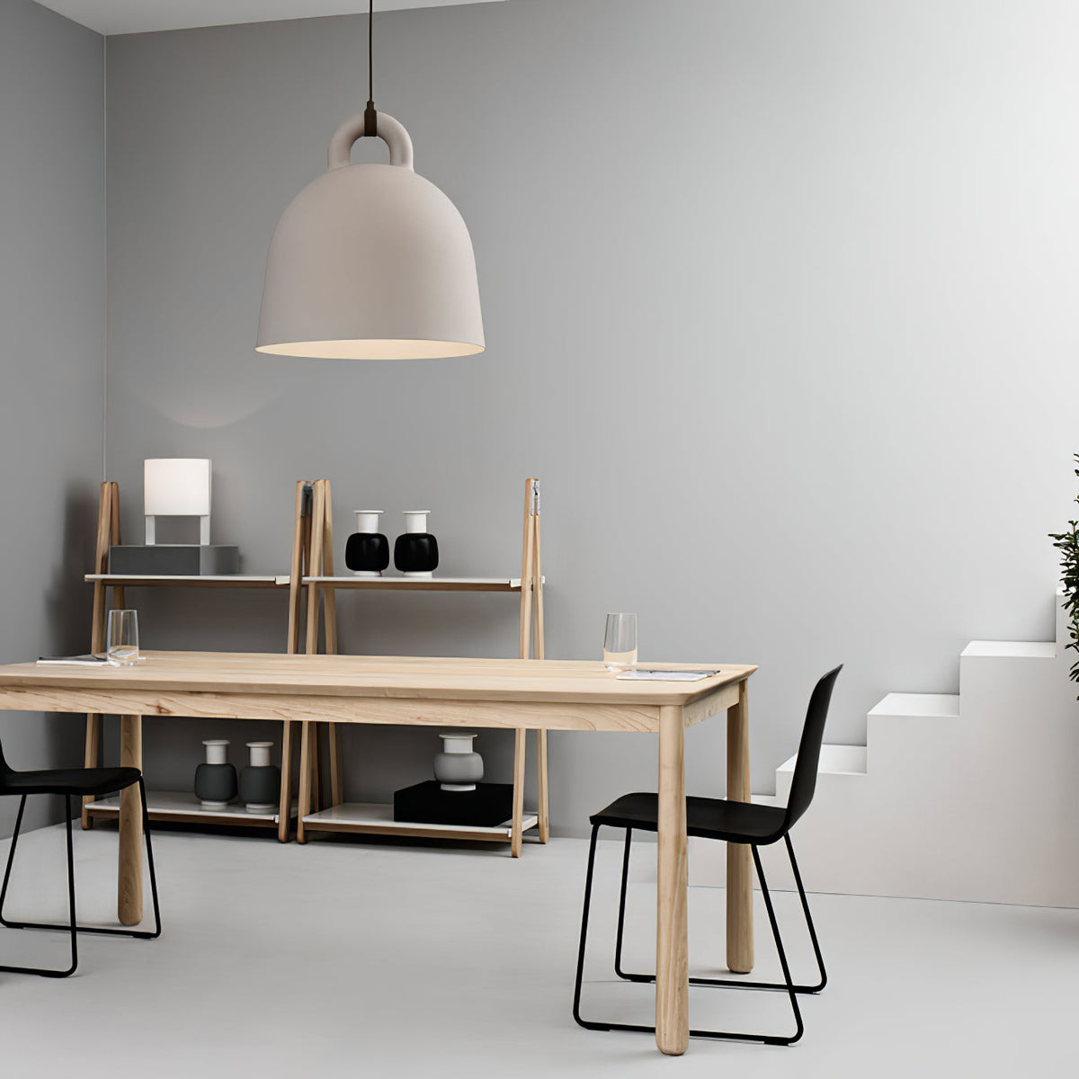 A large sand-coloured Clérachic bell pendant hangs over a pale wood table, with a shelving unit and black chairs behind it.
