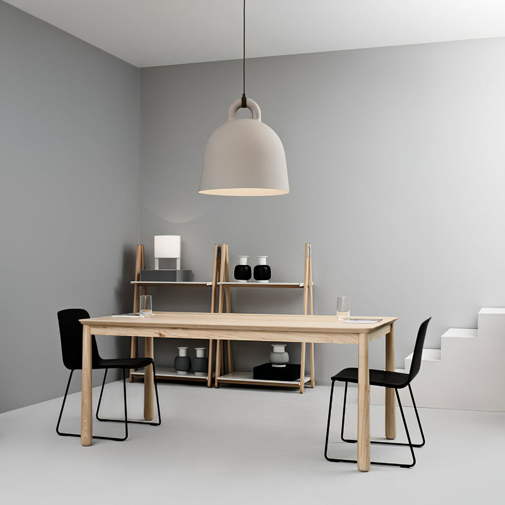 A sand-coloured Clérachic bell pendant hangs in a grey room with a pale wood table, black chairs and a shelving unit.