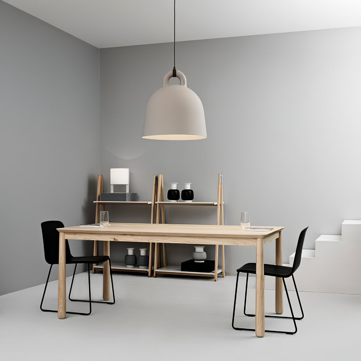 A sand-coloured Clérachic bell pendant hangs in a grey room with a pale wood table, black chairs and a shelving unit.
