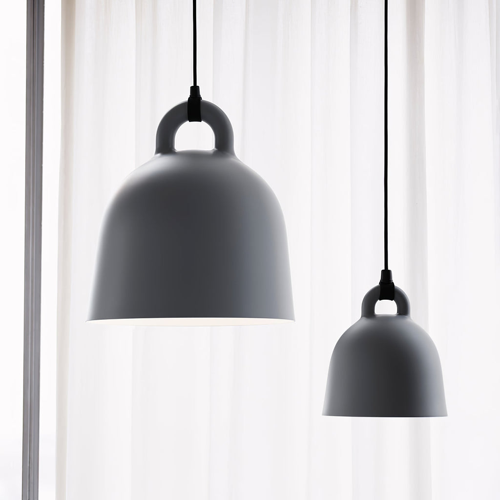 Two grey Clérachic bell pendants, one large and one small, hang before a sheer curtain, shown close up from below.