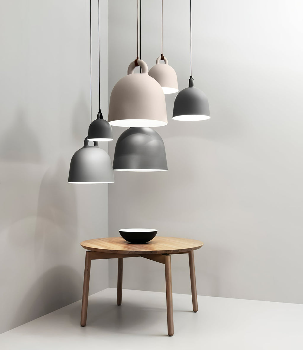 Five Clérachic bell pendants in grey and sand hang over a round wooden table with a black-and-white bowl, in a grey corner.