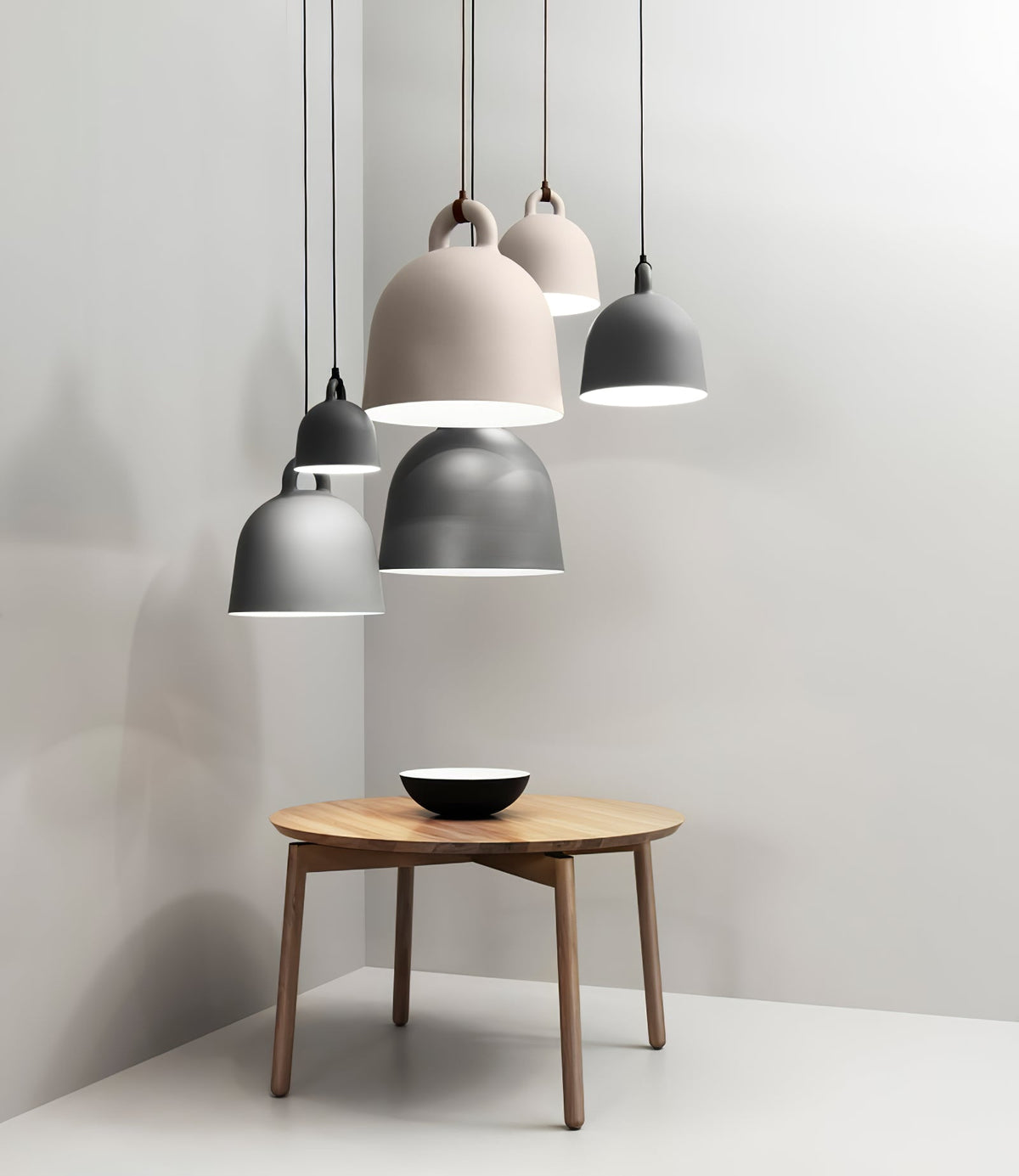 Five Clérachic bell pendants in grey and sand hang over a round wooden table with a black-and-white bowl, in a grey corner.