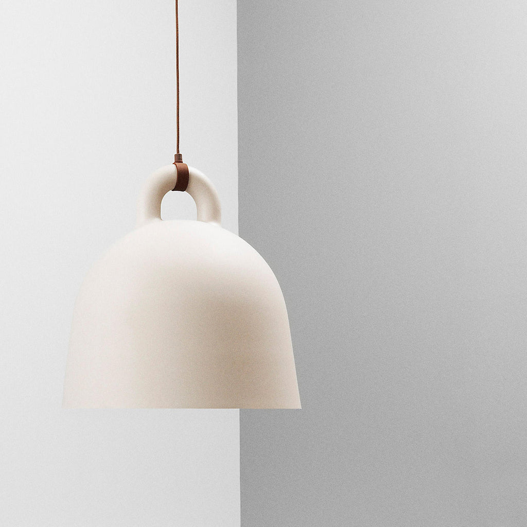 A cream Clérachic bell pendant with a brown cord hangs against a pale grey wall that meets a lighter panel.