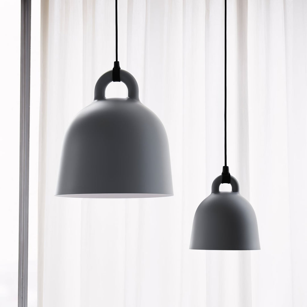Two grey Clérachic bell pendants, one large and one small, hang before a sheer white curtain, shown from below.