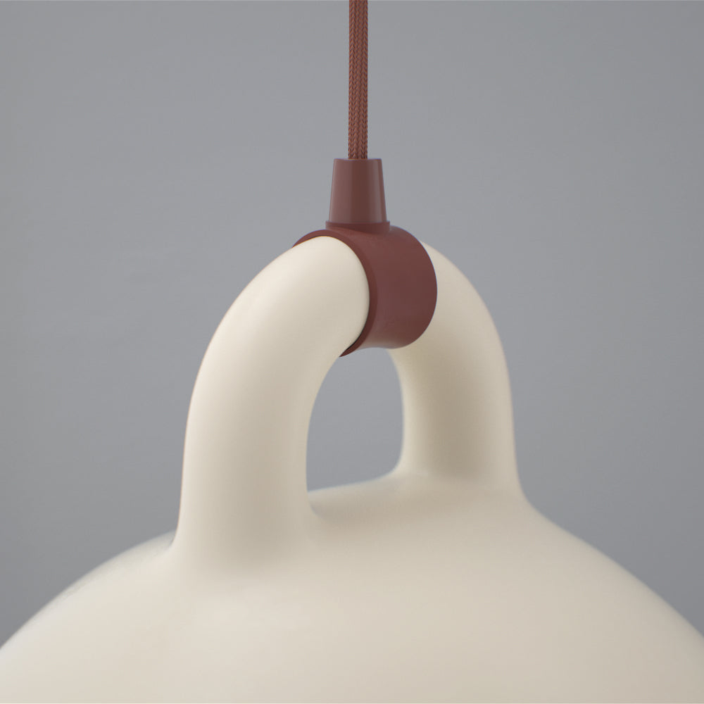 Close view of the loop handle and brown cord fitting on a sand-coloured Clérachic bell pendant, on a grey backdrop.