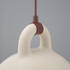 Close view of the loop handle and brown cord fitting on a sand-coloured Clérachic bell pendant, on a grey backdrop.