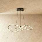 Clérachic pendant of interlaced LED loops in black on three thin cables, glowing against a limewashed wall and ceiling.
