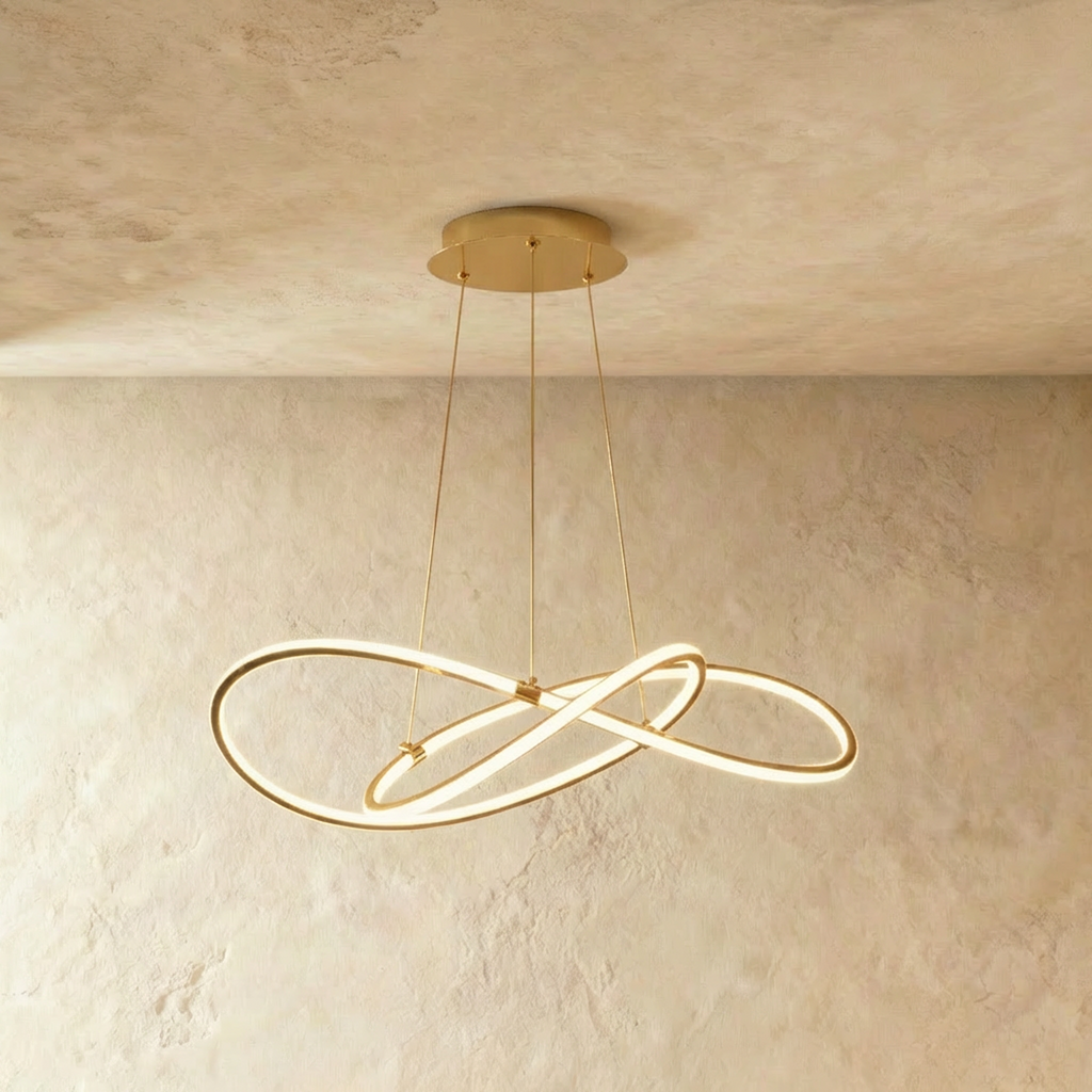 Clérachic brass-finish pendant of interlaced LED loops on three slim brass cables, lit against a textured plaster wall.