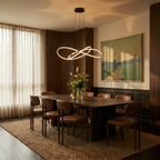 Clérachic black LED loop pendant above a long walnut dining table, set in a warm room with sheer curtains and a landscape painting.