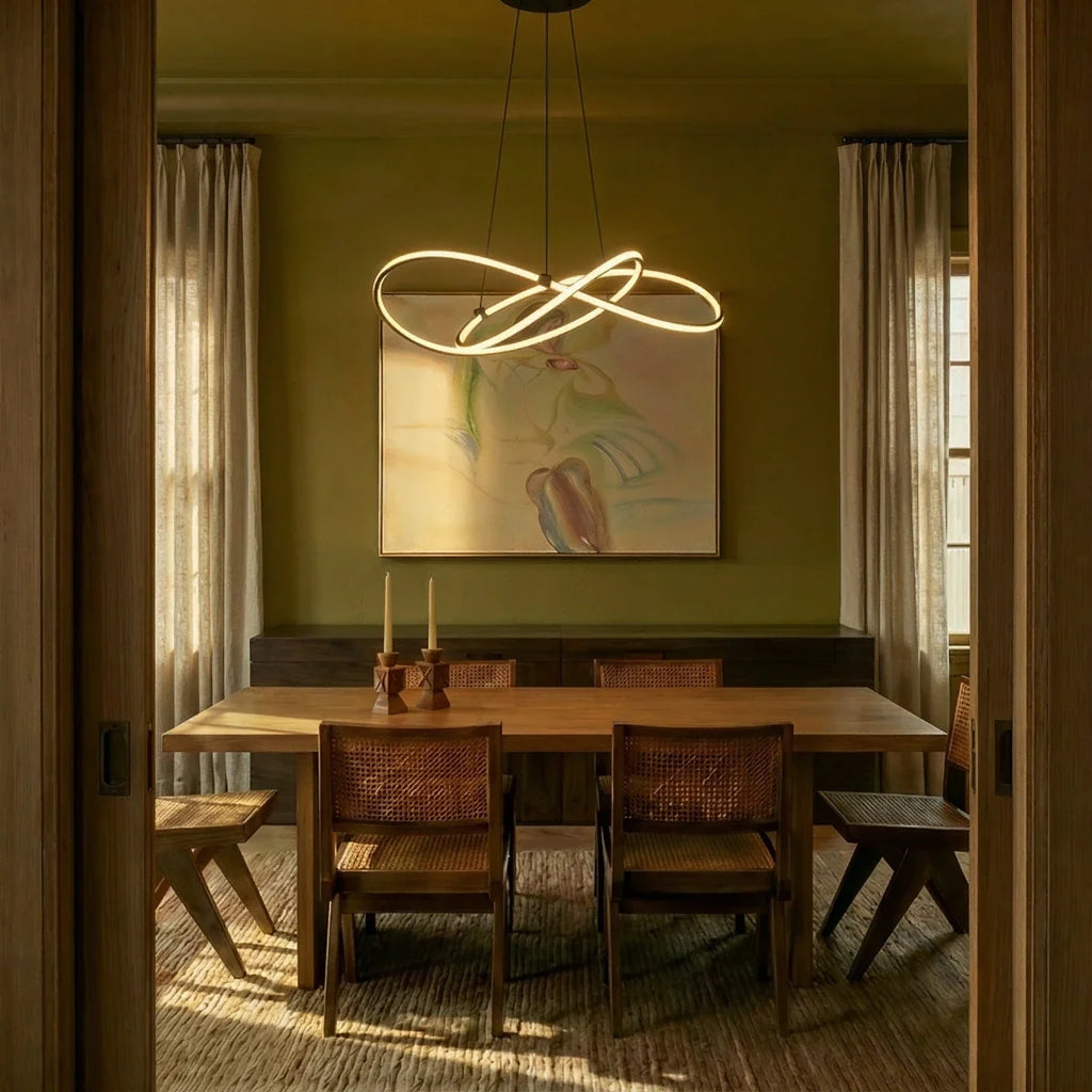 Clérachic black LED loop pendant over a timber dining table with cane chairs, in an olive green room lit by low sun.