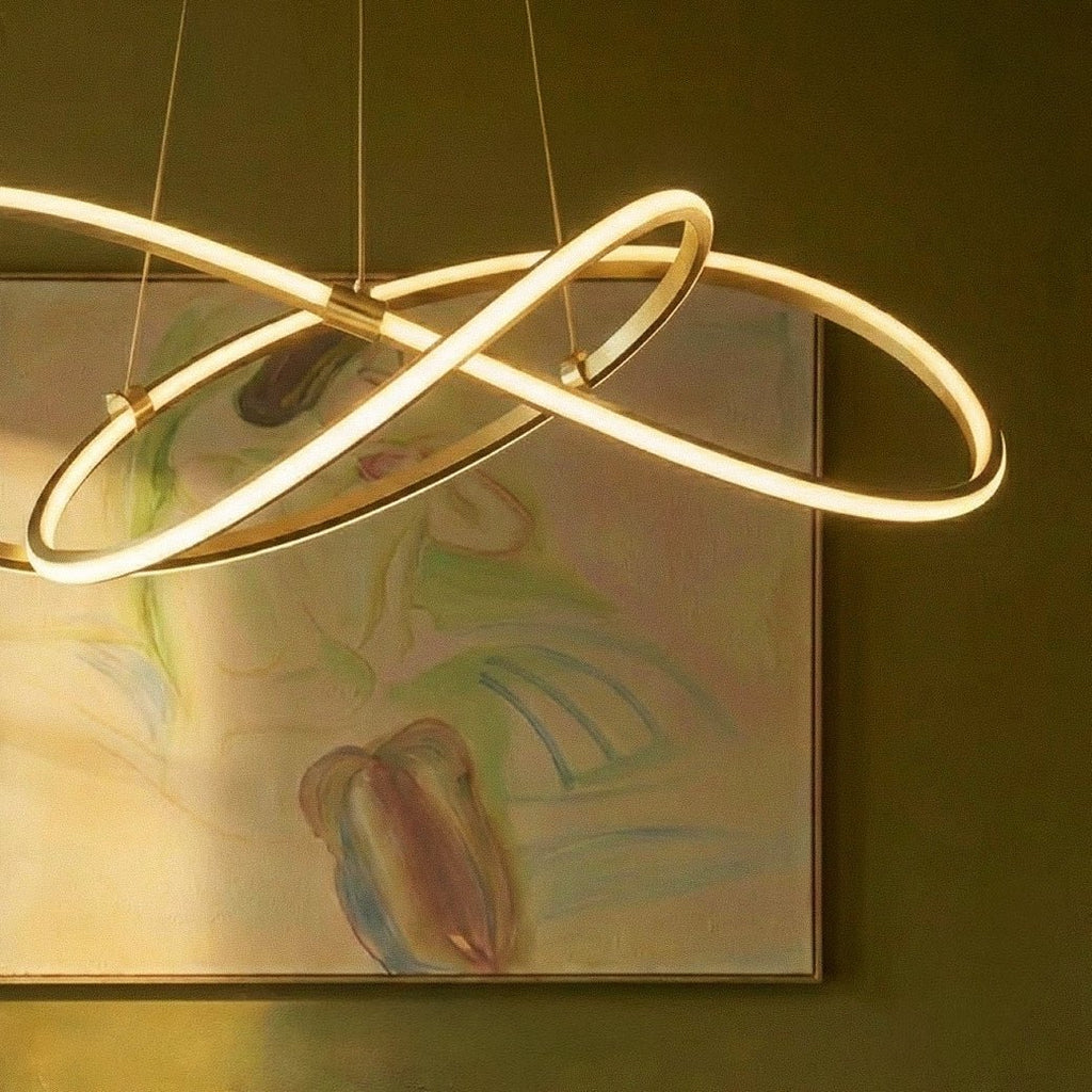 Close detail of the Clérachic brass pendant, its glowing loops and brass clamps set against an abstract painting.