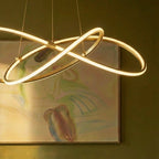 Close detail of the Clérachic brass pendant, its glowing loops and brass clamps set against an abstract painting.