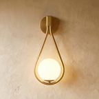 Clérachic gold iron arm wall sconce with a teardrop frame cradling an opal glass globe on a plaster wall.