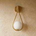 Clérachic gold iron arm wall sconce shown straight on, its teardrop frame glowing around an opal glass globe.