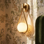 Close view of the Clérachic gold iron arm sconce's teardrop frame and opal glass globe against floral wallpaper.