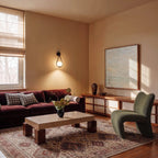 Clérachic black iron arm wall sconce glowing in a living room corner beside a velvet sofa and framed artwork.