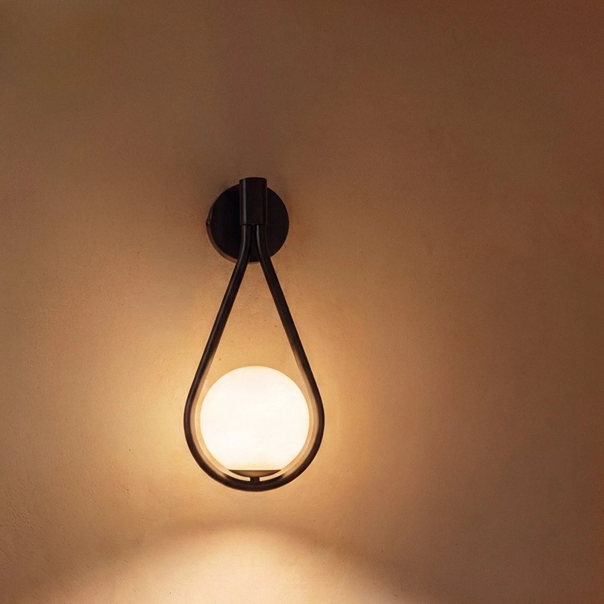 Close view of the Clérachic black iron arm sconce, its teardrop frame glowing around the opal glass globe.
