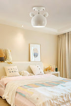 Small white Clérachic ceiling lamp lit in a warm bedroom with a pastel quilt, cushions and a framed print.