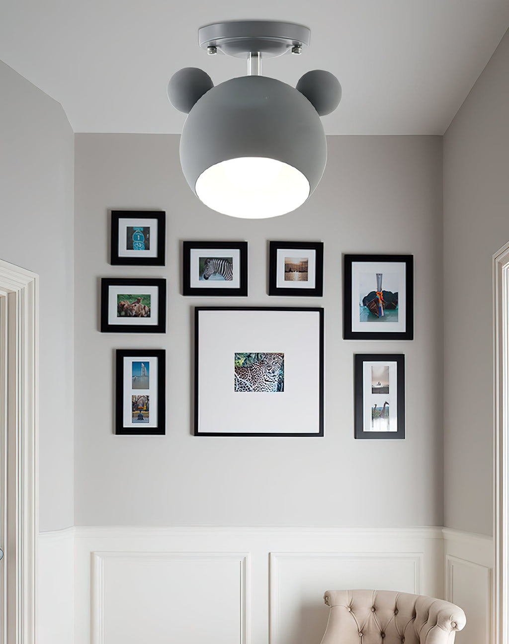 Grey Clérachic ceiling lamp lit in a hallway nook, above a gallery of black-framed pictures on a grey panelled wall.