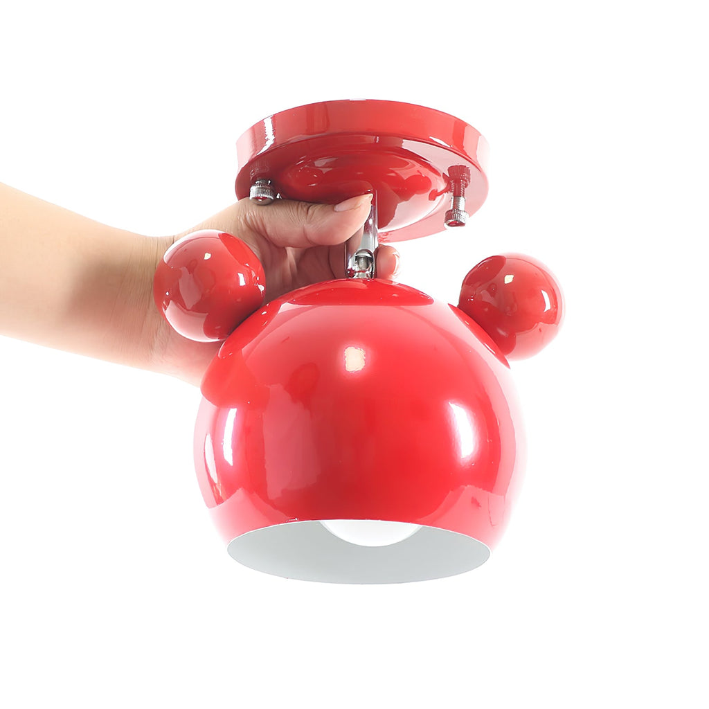 A hand holds the red Clérachic ceiling lamp, showing how compact the glossy dome and round ears are.
