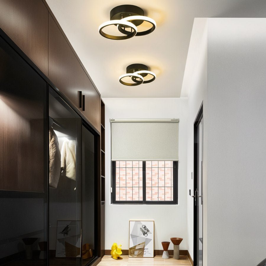 Clérachic two black twin-ring ceiling lights glowing warm along a narrow hallway beside dark wardrobes and a small window.
