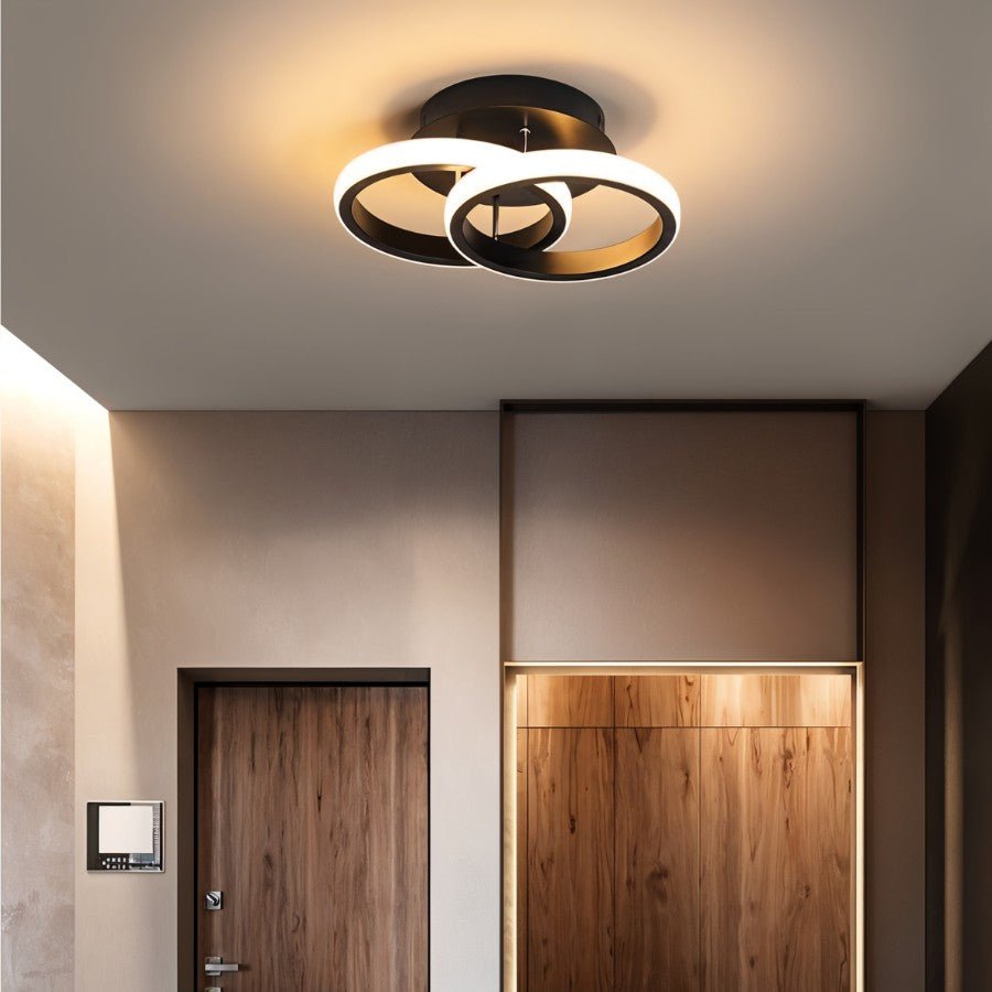 Clérachic black twin-ring ceiling light glowing warm above an entrance hall with a walnut door and a lit timber alcove.
