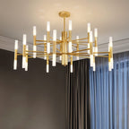 Clérachic gold multi-tier chandelier with glowing frosted tubes, hung in a room with dark walls and blue sheer curtains.