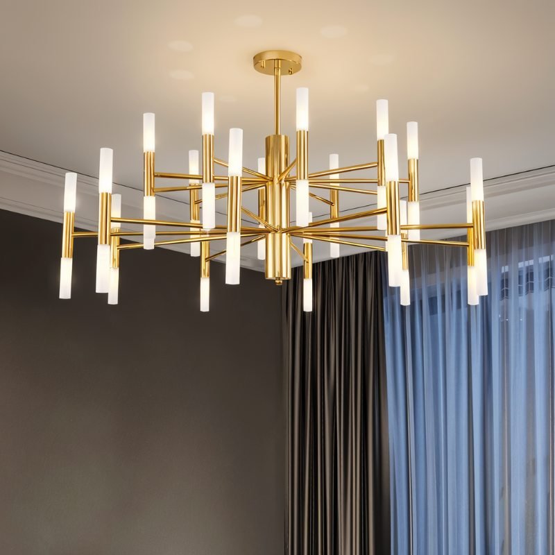 Clérachic gold multi-tier chandelier with glowing frosted tubes, hung in a room with dark walls and blue sheer curtains.