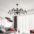 Clérachic black two-tier chandelier lit above a grey sofa and red cushions in a bright, white living room.