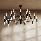Clérachic black multi-tier chandelier lit against a textured plaster wall, with soft window shadows across it.