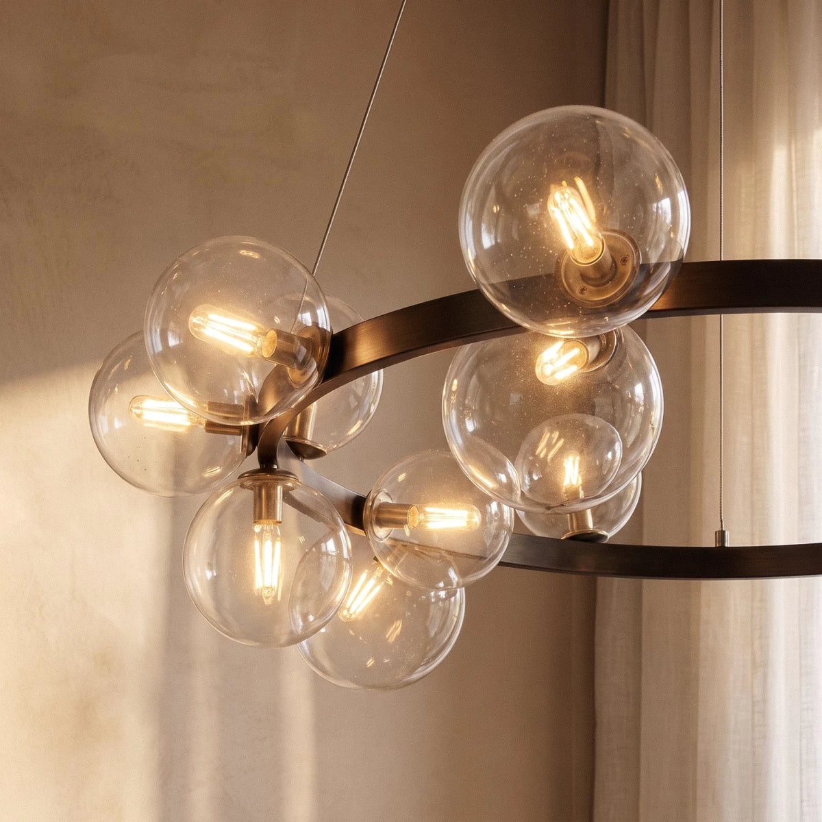 Detail of the Clérachic ring chandelier's brass bulb fittings and clear glass globes against sheer curtains behind.