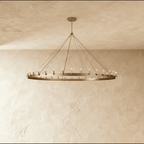Clérachic wide brass ring chandelier with slim candle-style bulbs and fine rods, hung against a limewashed plaster wall.