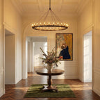 Clérachic wide matte black ring chandelier lit above a round pedestal table in a grand panelled entrance hall.