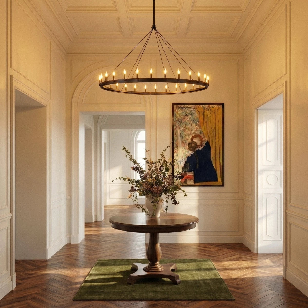Clérachic wide matte black ring chandelier lit above a round pedestal table in a grand panelled entrance hall.